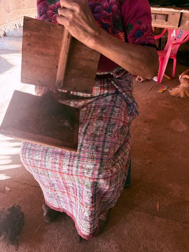 Un artesano guatemalteco, con vestimenta tradicional maya, utiliza cardas manuales de madera
