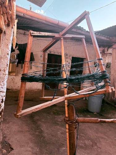 Devanador tradicional de madera enrollando hilo de lana oscura en un patio rústico al aire libre.