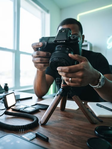 Dynamic low-angle shot of a professional camera setup on a desk, high-quality mirrorless camera, hands adjusting a lens, bright natural daylight mixed with subtle electric lime neon accents, 35mm lens, modern editorial photography.