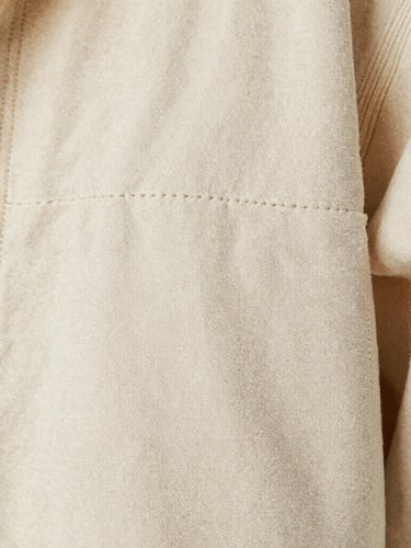 Tight macro shot of double-stitched seams on a heavy cream canvas jacket, showing tactile fabric weave, soft natural light