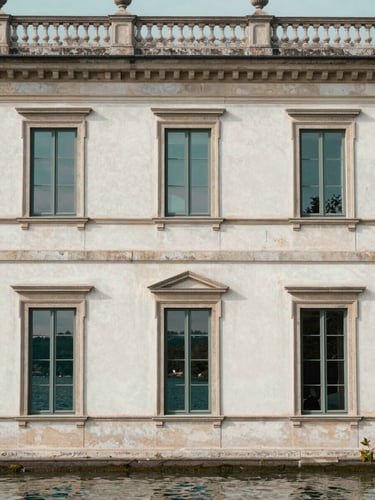 Elegant medium shot of a historic villa facade with stone details, soft natural lakeside light reflecting on the windows, warm white and deep teal tones, elegant editorial photography, architectural symmetry, medium format