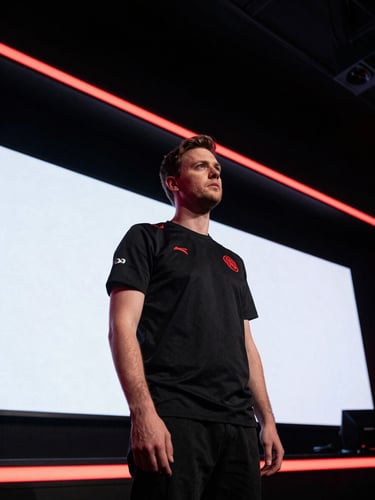 Dramatic low-angle shot of a professional esports coach standing in front of giant arena screens, sharp red rim light, 35mm focus