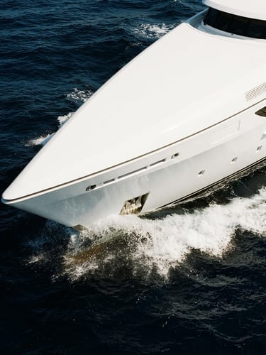 Architectural crop of a pristine white yacht hull slicing through deep blue water under bright, high-contrast coastal daylight.