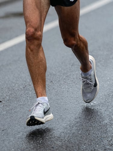 Close-up dynamic crop of a runner's legs mid-stride on wet Detroit asphalt, overcast morning light, silver highlights, focused and raw.