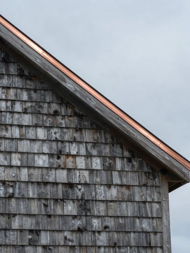 Overcast coastal daylight shot of a weathered cedar shingle home exterior with clean copper flashing details along the roofline.