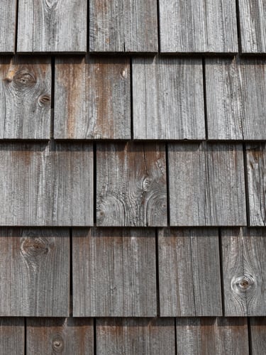 Tight close-up of interlocking cedar shake siding, showing the raw weathered wood grain and tight joints, coastal Connecticut.