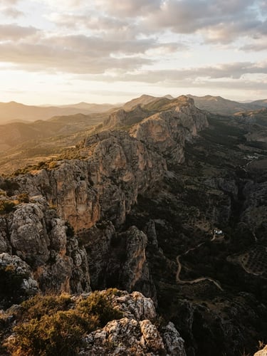 Atmospheric 35mm film shot of the limestone cliffs of Serranía de Ronda, golden hour light casting long dramatic shadows, rugged mountain ridges, environmental scale.