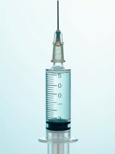 Macro clinical photograph of a clear glass syringe filled with viscous fluid, sterile laboratory lighting with medical cyan backlighting, sharp focus, 50mm