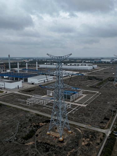 Aerial drone orthographic photograph of a graded industrial land parcel with high-voltage transmission towers, technical layout lines overlaid, overcast daylight, cool desaturated tones