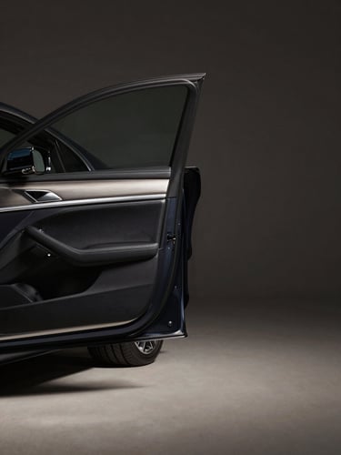Wide environmental shot from low angle, interior driver-side door panel of a premium dark sedan, brushed metal handle and stitched leather trim in sharp focus, studio lighting with a single directional source from upper left casting clean shadows, neutral dark background, generous negative space on the right third of the frame
