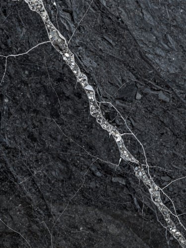 A massive slab of dark charcoal granite with intricate white quartz veining, shot from a straight-on angle, high-contrast lighting emphasizing the polished surface and natural mineral depth.