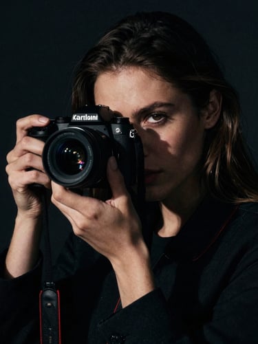 An intense close-up portrait of photographer Kira Sadian holding a camera, dramatic side-lighting with deep chiaroscuro shadows, dark obsidian background, cinematic 35mm