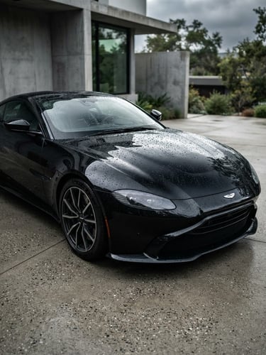 Sleek black luxury sports car parked in a minimalist concrete driveway, high-contrast studio-style lighting reflecting off the pristine hood, water beading sharply, 50mm lens