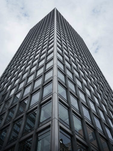 Wide low-angle architectural photograph of a modern steel and glass skyscraper facade, sharp geometric shadows, overcast daylight, minimalist composition.