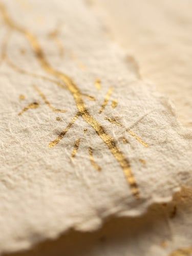 Close-up macro shot of handmade cotton paper texture with gold ink lines, warm diffused side-lighting, shallow depth of field