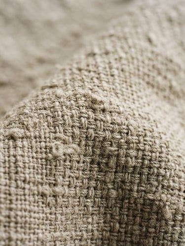 Extreme close-up of stone-washed linen fabric texture, soft natural morning light, neutral plaster background, minimalist editorial style, 35mm film grain