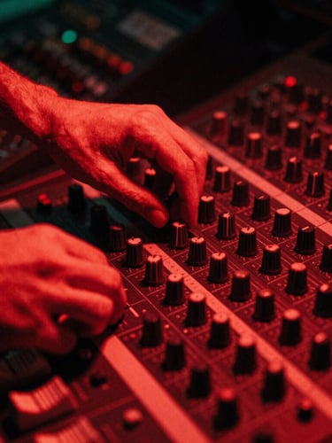 Close-up of hands adjusting dials on a vintage mixing console in a dark studio, harsh red neon light casting deep shadows, 35mm grain