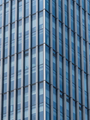 Crisp architectural photography of a modern high-rise glass facade with sharp geometric lines, cool daylight reflecting subtle royal blue tones, clean corporate minimalism.