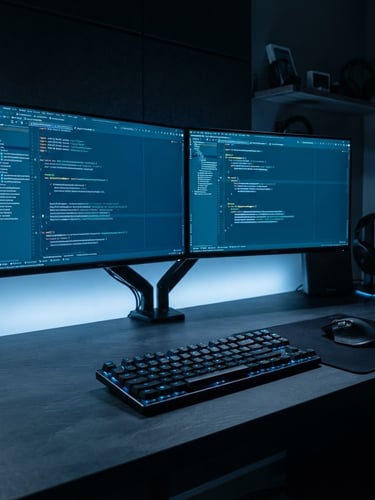 Wide organized developer workspace, dual monitors displaying clean Android Studio code on dark screens, cool blue edge lighting from the left, sharp focus on keyboard and screen, deep slate desk surface, no clutter