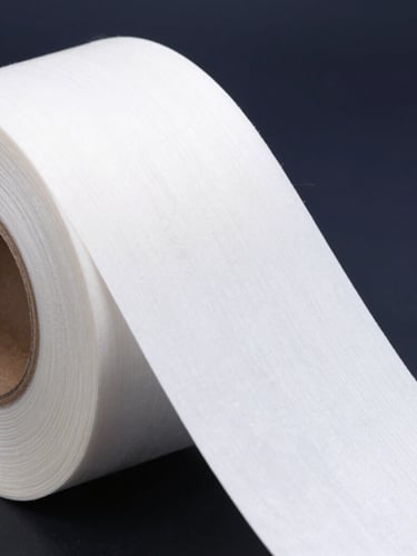 Macro shot of a high-contrast white thermal label being peeled off a roll, showing strong adhesive fibers stretching, cool dark navy background, sharp studio lighting