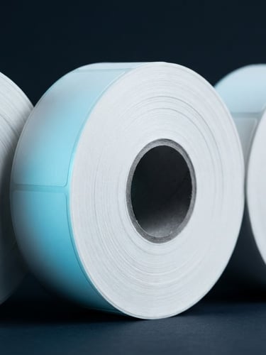 Close-up of pristine thermal label rolls on a dark background, sharp cyan studio highlights, macro photography, 50mm lens