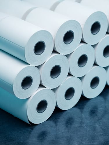 Macro photograph of pristine white thermal label rolls on a dark metallic surface, cool studio lighting with sharp cyan highlights, 50mm lens