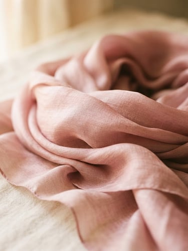 Warm editorial photography of a beautifully draped dusty pink silk scarf catching soft window light, cream background, shallow depth of field, 35mm