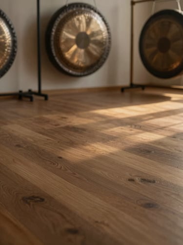 Wide environmental shot of an empty serene studio space with natural textures like wood and raw linen, a large bronze gong in the background, soft golden-hour light streaming in from the right.