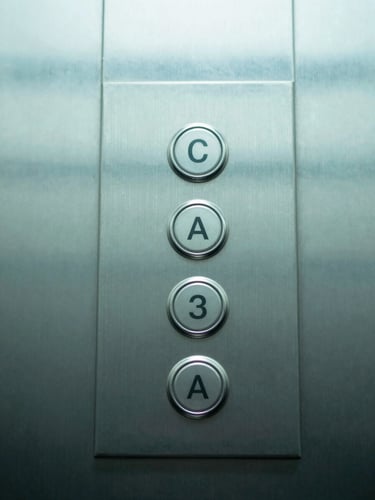 Macro shot of a sanitized metal elevator button panel in a corporate building, sharp focus, clean white overhead office lighting, sterile mint-teal accents.