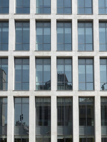 Symmetrical wide shot of a modern corporate building facade with clean glass panels, bright daylight, sterile architectural lines.