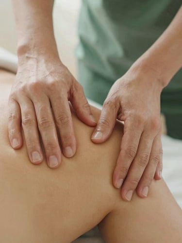Close-up of therapeutic hands performing targeted massage on a shoulder, soft diffused daylight, warm wood tones, earthy forest green accents, shallow depth of field, 35mm