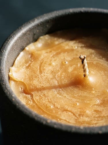 A macro close-up of warm golden hand-poured candle wax setting in a dark ceramic vessel, dramatic side lighting, deep slate background, 35mm