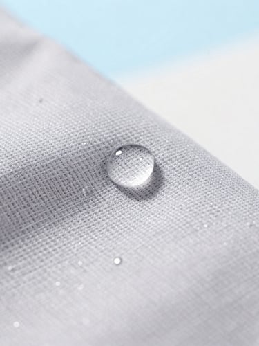 Macro close-up of water droplets beading perfectly on soft grey woven fabric, bright natural daylight, clean airy background, 35mm lens.