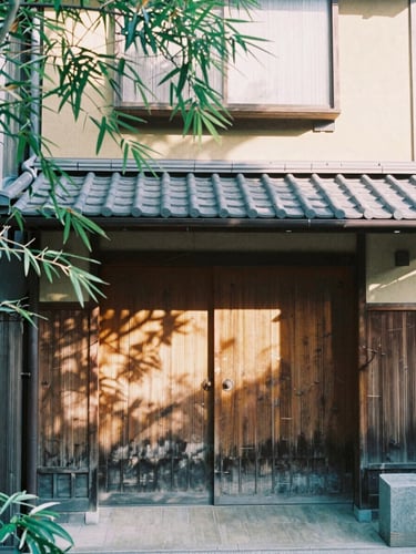 A serene morning view of a traditional wooden machiya townhouse entrance in Kyoto, soft sunlight filtering through bamboo leaves, 35mm film look