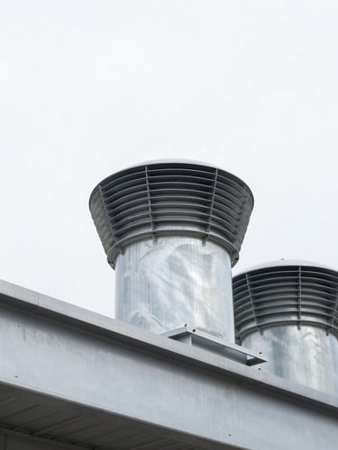 Low-angle architectural shot looking up at installed industrial roof vents against a crisp, bright overcast sky, sharp metal edges, 35mm