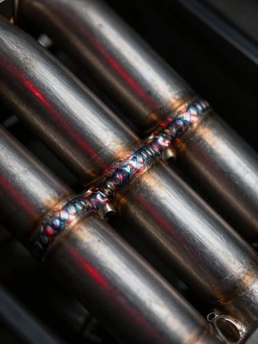 Macro shot of a custom titanium exhaust manifold with precise TIG welds, low-key lighting, dramatic red highlights reflecting off the metallic surface.