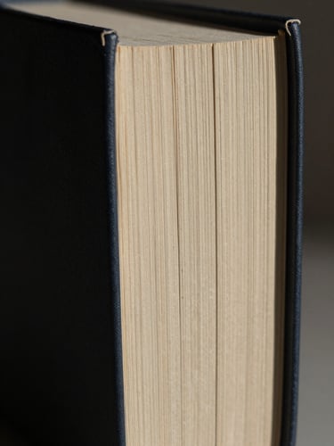 Extreme close-up of heavy physical book spines with deep textured paper, harsh directional lighting casting stark shadows, tactical minimalist layout.