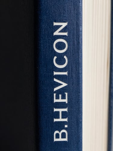 Extreme close-up of a physical book spine with clean typography and deep navy blue linen texture under high-contrast directional shadows.