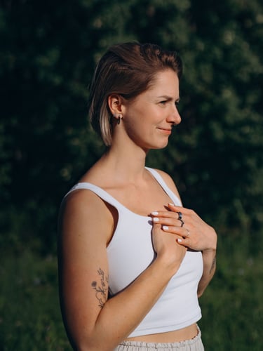 A woman in a white tank top practices mindfulness meditation outdoors in nature.