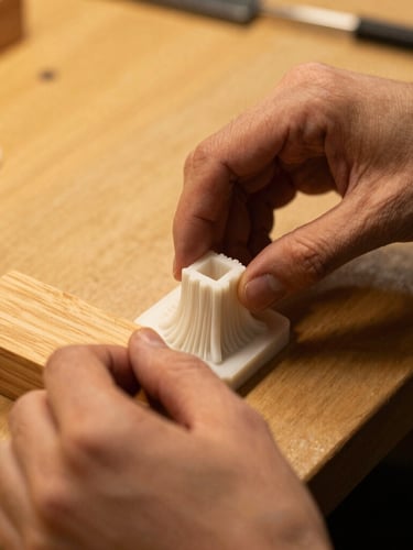 Close-up portrait shot of hands carefully placing a 3D printed part next to a wooden component on a workbench, warm amber side-lighting, rich textures, shallow depth of field, 35mm.