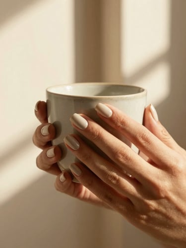 Close-up of hands with detailed press-on nails holding a ceramic cup, soft shadows, warm editorial photography