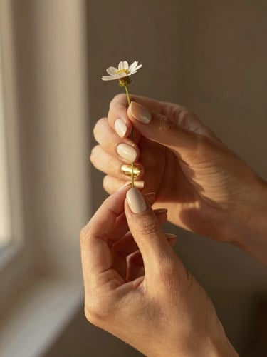 A close-up of hands with minimalist neutral cream and gold-accented press-on nails gently holding a delicate wildflower