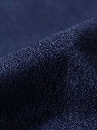 Macro close-up of premium dark navy cotton weave, bright directional light highlighting the fine textile fibers and flawless double-stitch line, minimalist composition.