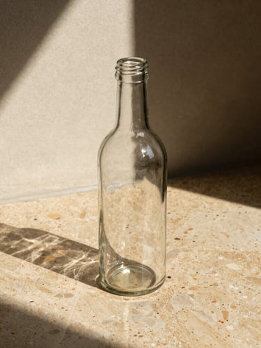 Refillable heavy glass bottle casting sharp afternoon shadows on warm travertine stone, direct sunlight, high contrast, 35mm