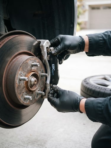 Close-up of clean, professional mechanic hands installing fresh brake pads on a car wheel, bright natural outdoor daylight, tidy concrete driveway background, sharp focus
