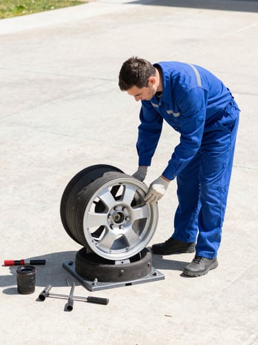 A professional mechanic in a clean blue uniform working on a car wheel assembly in a sunny driveway, tools organized nearby, high-contrast crisp daylight