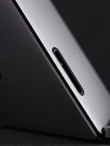 Extreme close-up of a MacBook Pro chassis showing the precise side ports and metallic texture, dramatic low-key studio lighting, dark background, zero clutter.