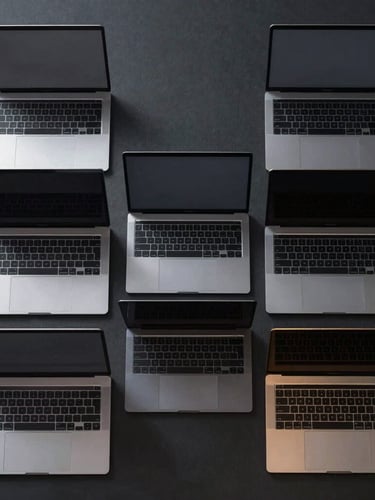 Symmetrical overhead shot of a fleet of sleek space-gray MacBook Pro laptops aligned perfectly on a dark matte surface, metallic edges catching gold light