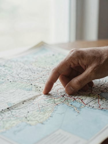 Editorial photojournalism, close-up of a hand tracing coordinates on a vintage physical map, soft natural window light, high contrast.