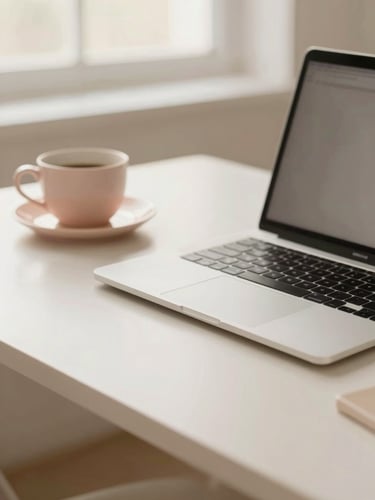An elegant, minimalist desk with high-end stationery, a sleek laptop, and a ceramic cup in soft morning window light, cream and blush tones, shallow depth of field.